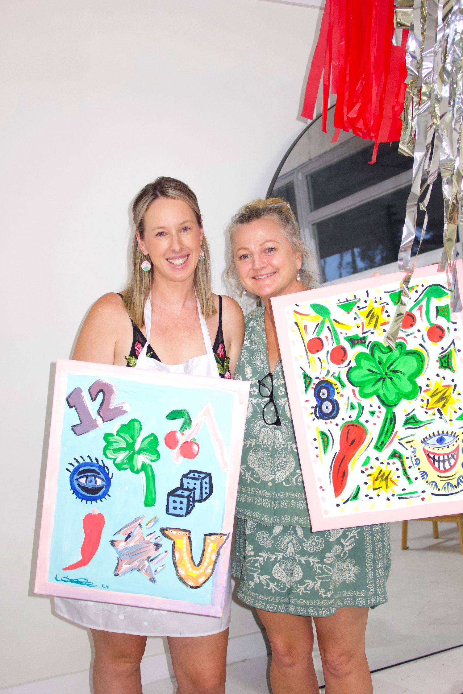 Two people holding up their colorful painted artwork at a creative workshop.