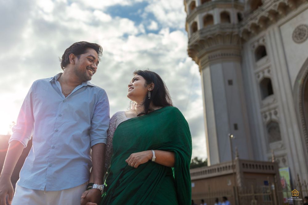 Couple posing against historic architecture with dramatic sunlit sky.