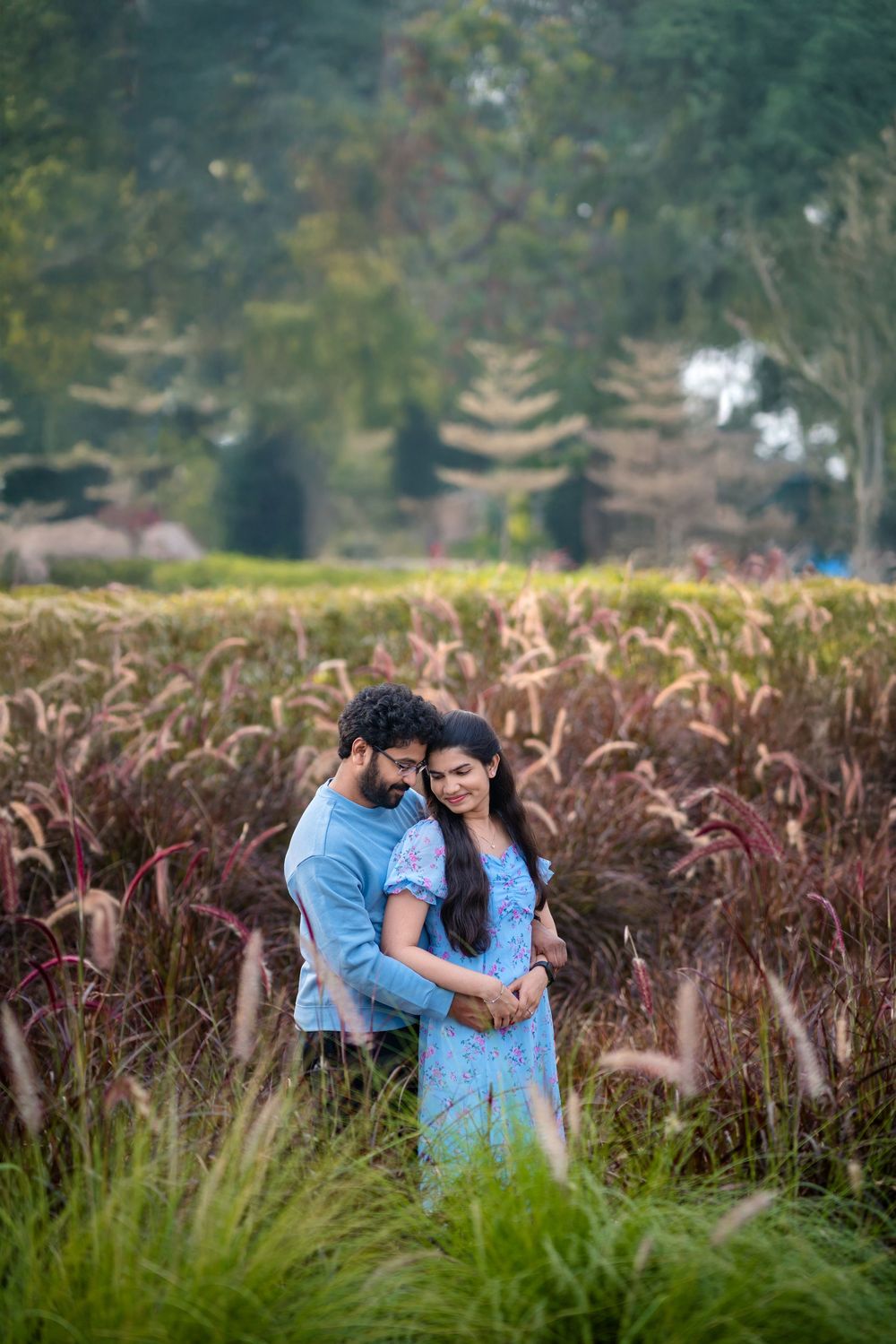 A couple shares an intimate moment among tall ornamental grasses in a garden setting.