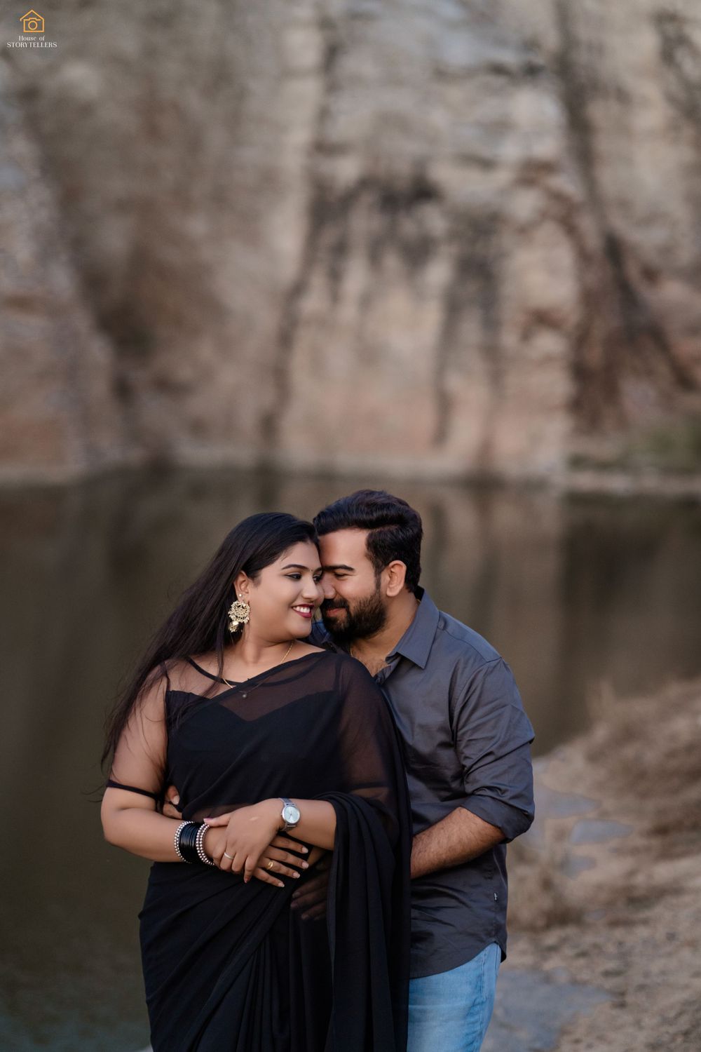 Intimate portrait of couple embracing by a lakeside with rocky backdrop.