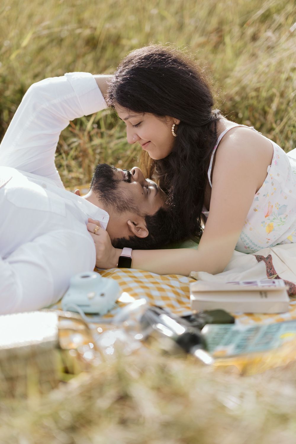 Couple sharing a romantic moment during a sunny outdoor picnic on a yellow checkered blanket in a grassy field.