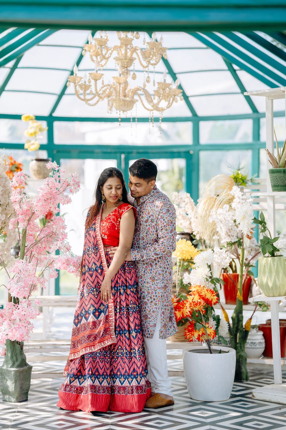 Couple in traditional Indian attire posing in greenhouse with floral decorations.