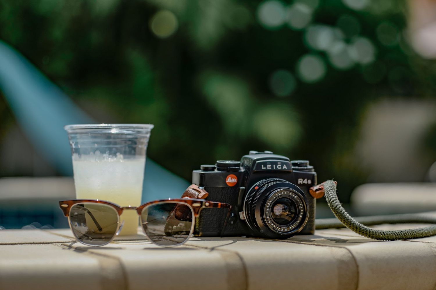 Vintage camera and sunglasses next to a half-empty drink glass on an outdoor table.