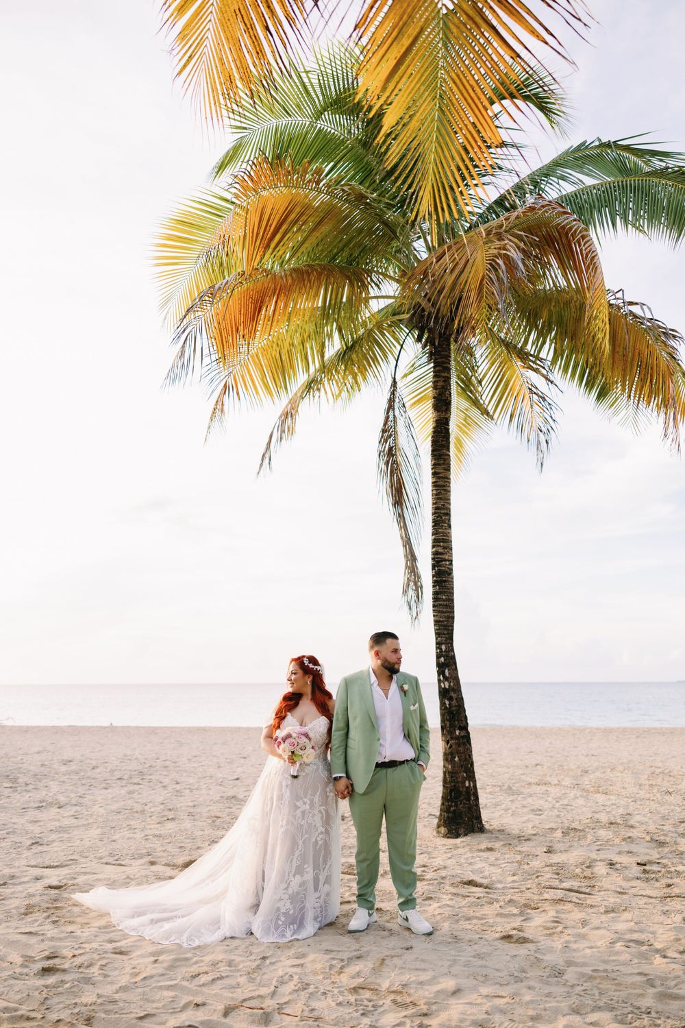 Wedding couple posing under a palm tree on a tropical beach.