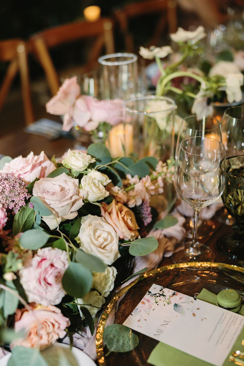 Romantic table setting with blush roses, eucalyptus, and crystal glassware on a rustic wooden surface.
