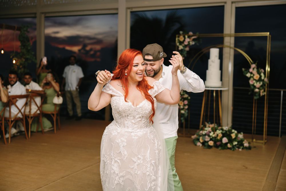 Joyful dance moment during wedding reception with glowing sunset through windows.