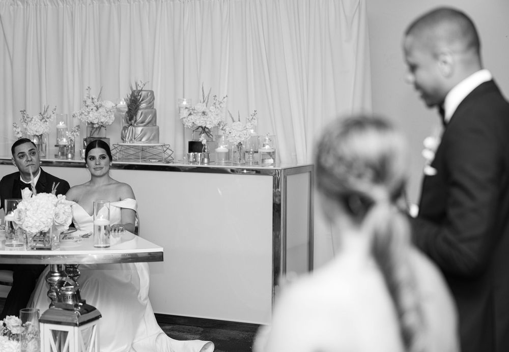 Black and white candid reception photo with guests at dining tables.