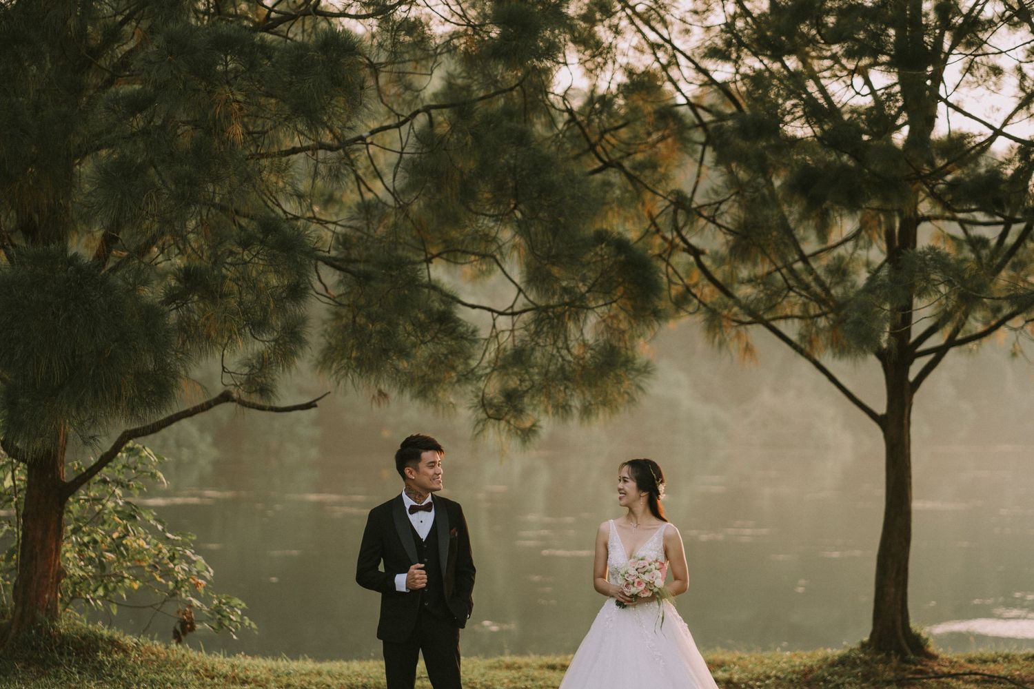 Wedding couple poses beneath towering trees in an outdoor setting.