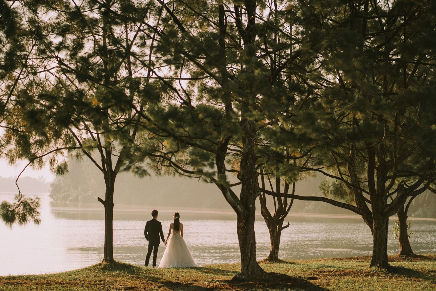 A romantic wedding photoshoot silhouetted against a misty lakeside landscape at sunset.