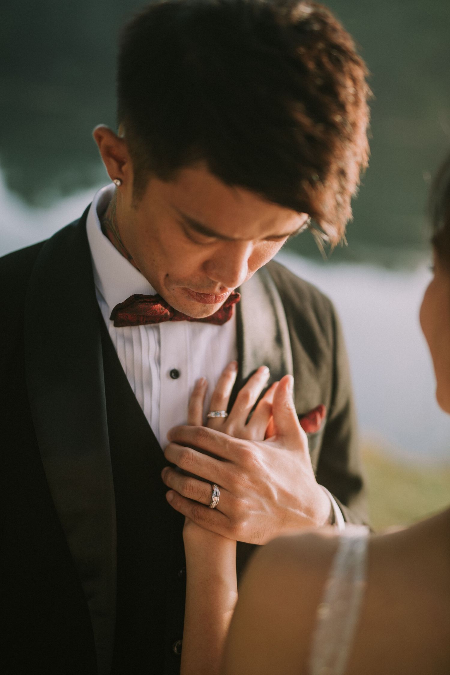 A close-up shot of clasped hands with wedding rings in formal attire.
