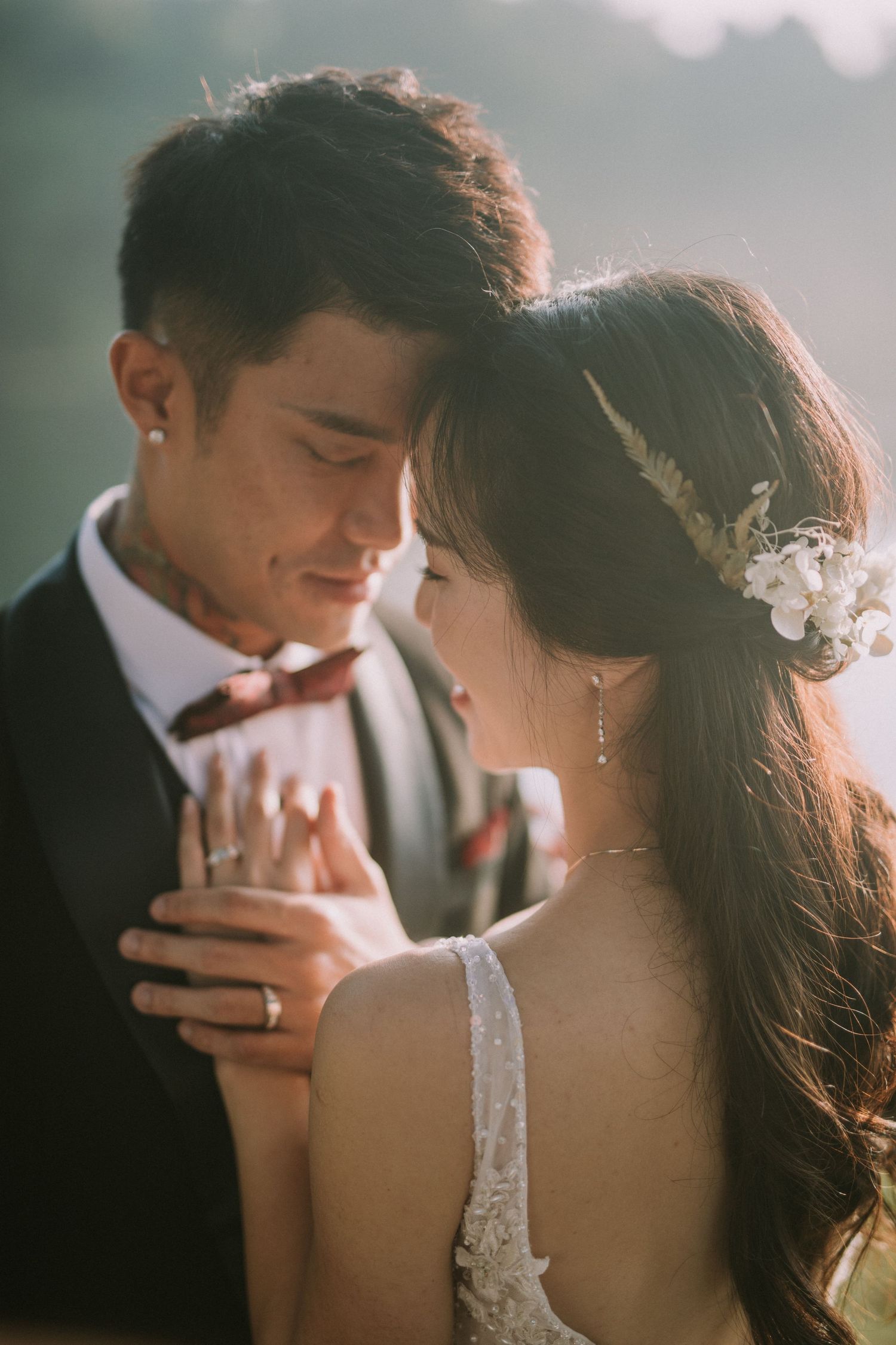Couple embraces tenderly in wedding attire with sunlit backdrop creating a dreamy atmosphere.