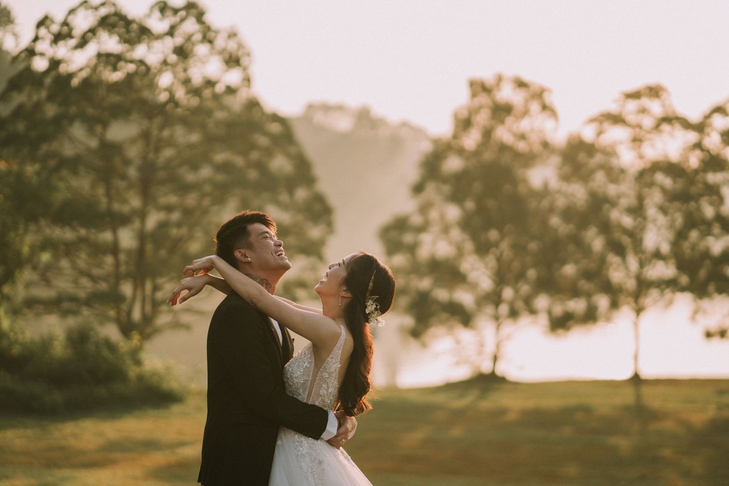 A couple in wedding attire embraces in a sunlit field during golden hour.