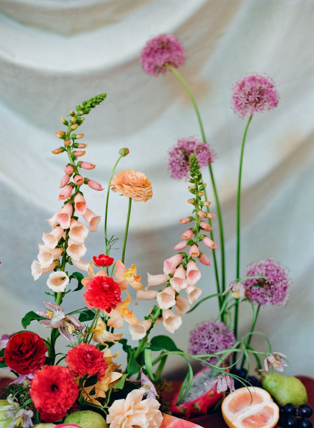 Elegant garden arrangement with pink snapdragons, coral ranunculus, and purple allium against a white backdrop.