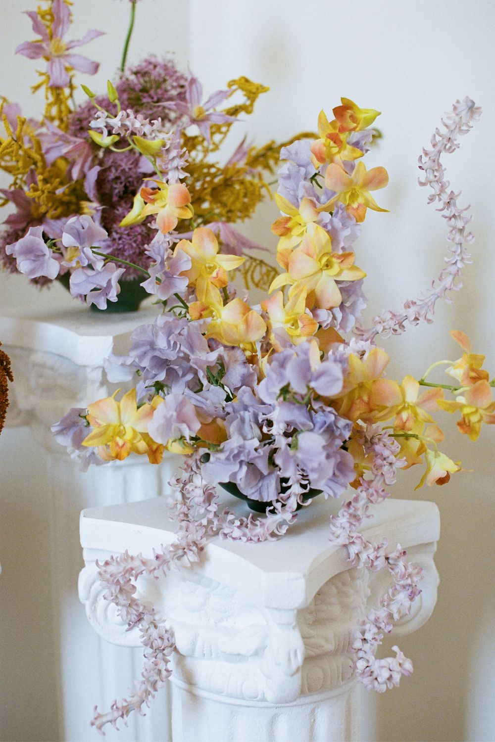 Luxurious floral arrangement with yellow orchids and pink astilbe displayed on a classical white column.