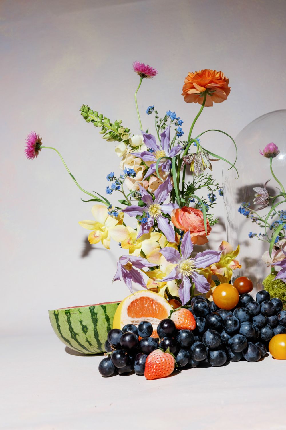 Colorful spring flower arrangement with watermelon, grapes, and citrus fruits on white background.