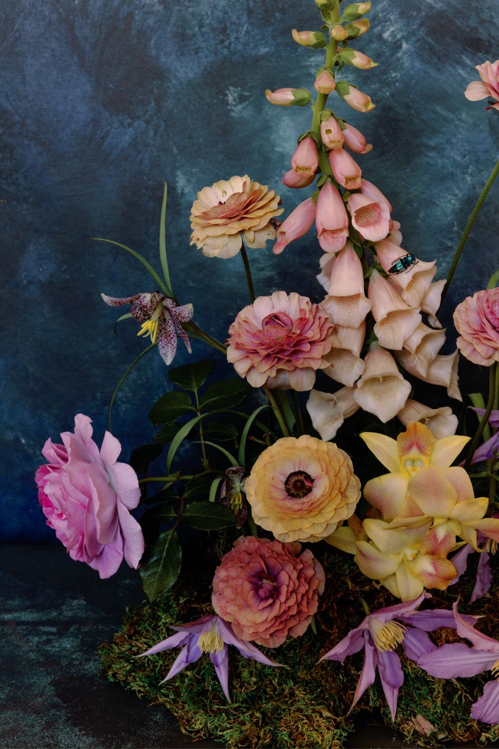 Dramatic floral arrangement with pink roses and foxgloves against deep blue textured background.