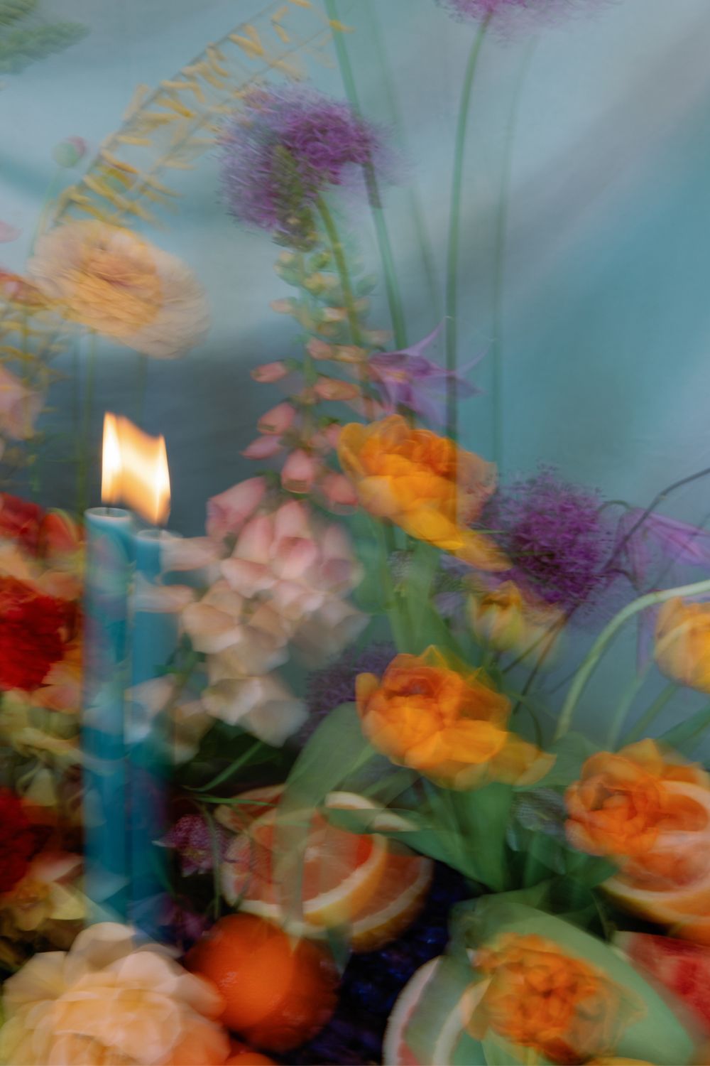Dreamy floral arrangement with blurred orange roses and blue candle creating an ethereal atmosphere.