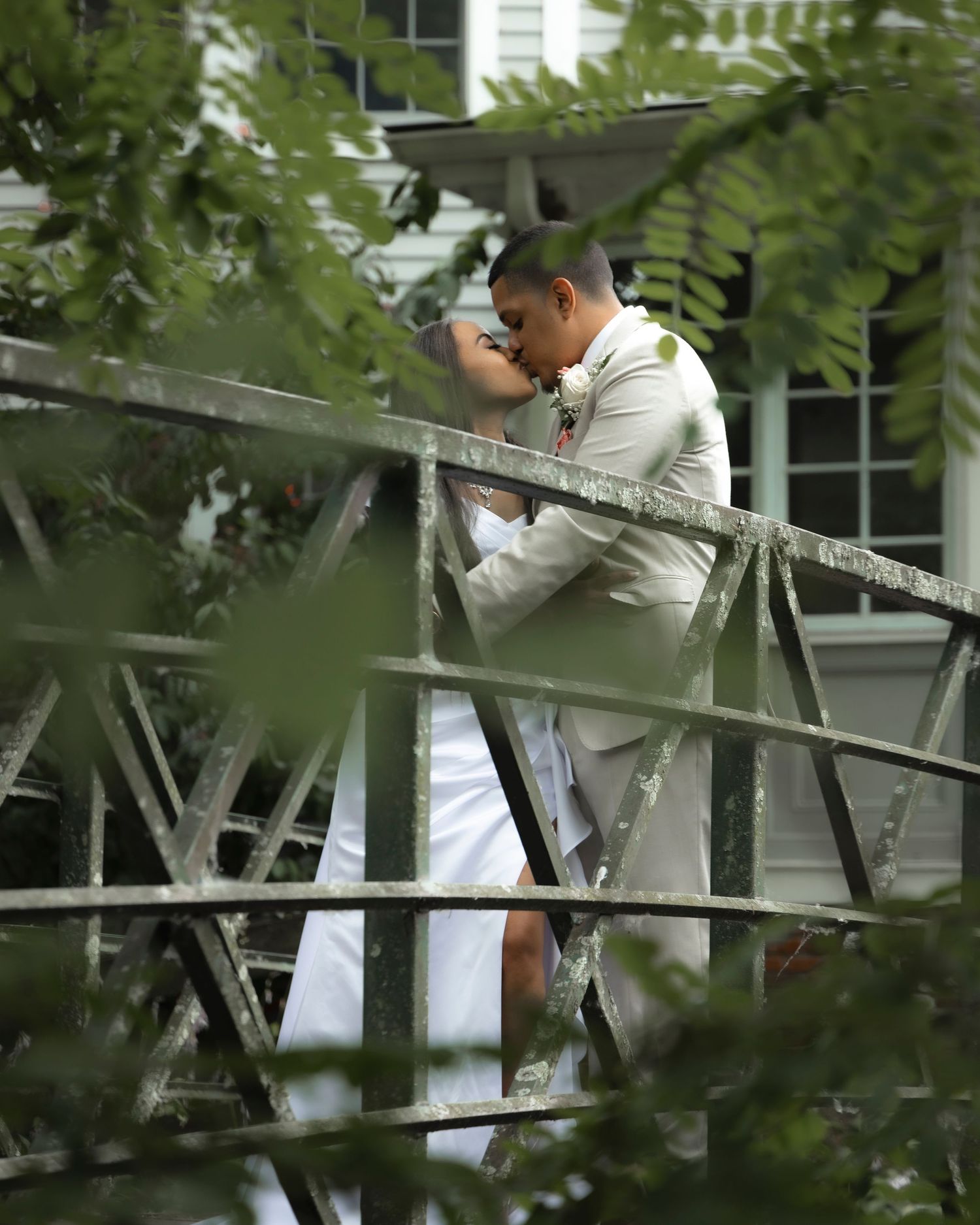 A wedding photo taken through foliage on a rustic bridge.