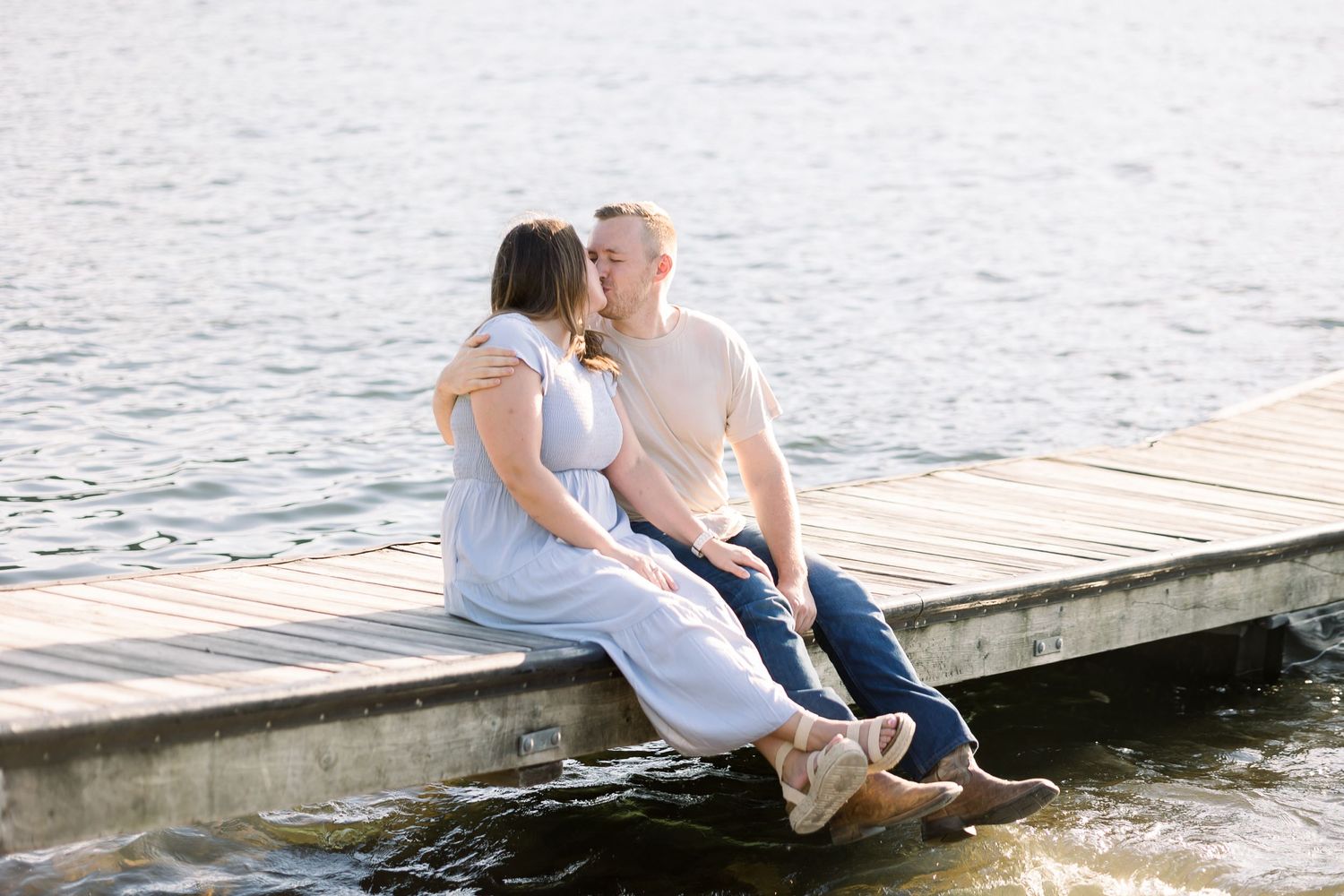 A couple sits close together on a wooden pier overlooking calm waters.
