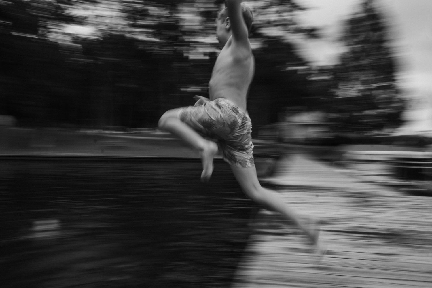 Motion-blurred black and white photograph captures a child leaping off a dock into a lake in Virginia