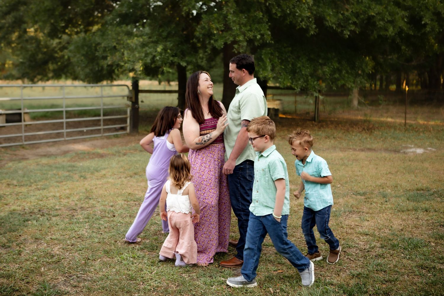 Pregnant woman and man pose outdoors with three young children during a family maternity photo session in a green park.