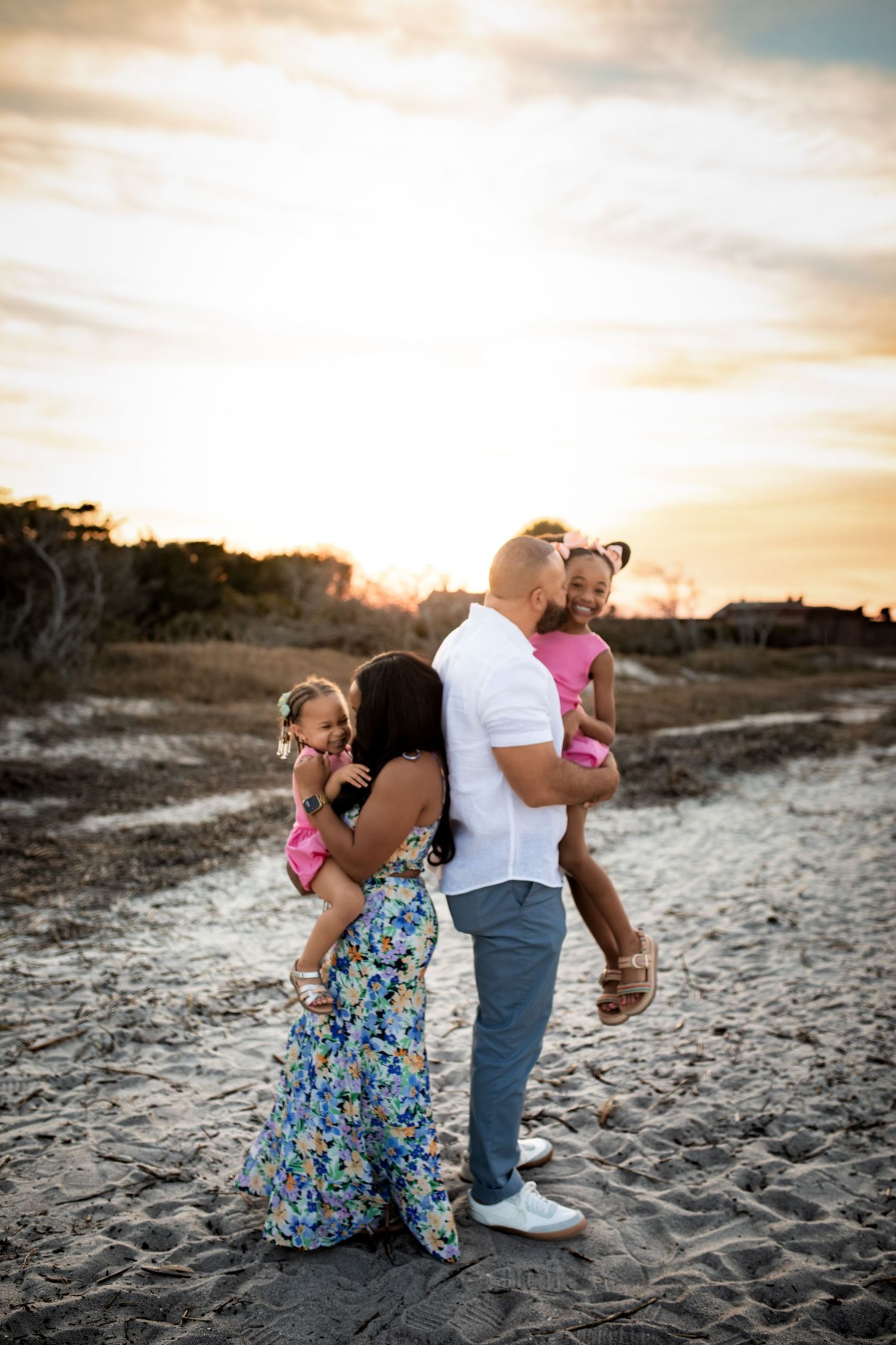 A family shares tender moments on a sandy beach at sunset as golden light illuminates the peaceful coastal scene.