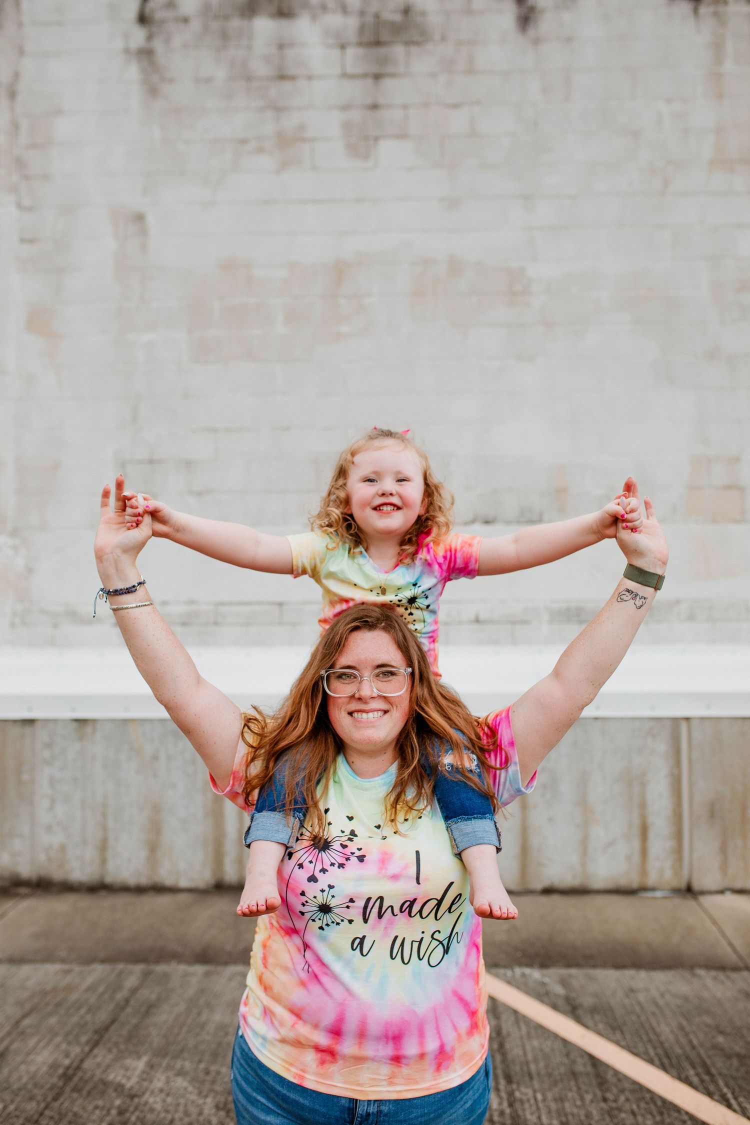 Joyful pair in tie-dye shirts having fun outdoors against concrete wall.