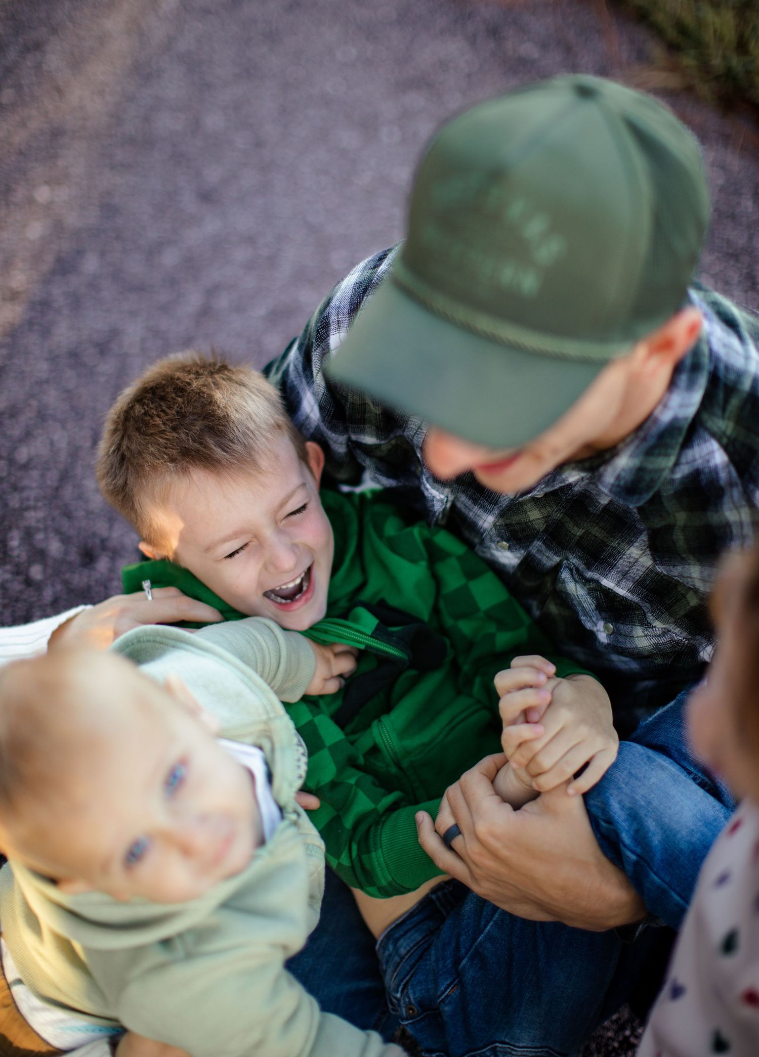 A playful outdoor moment captured with a child in green and an adult in a plaid shirt and baseball cap.
