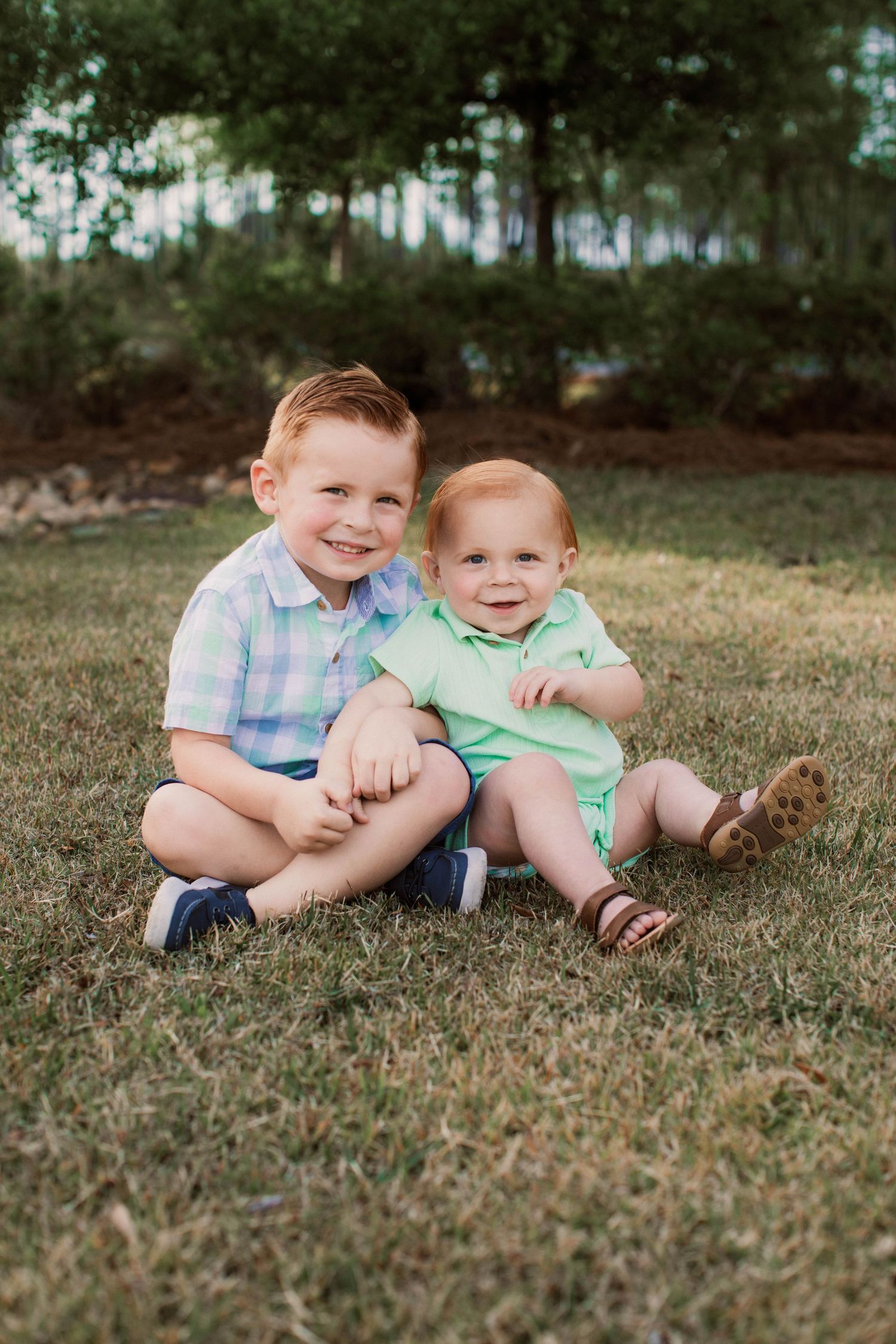 Two children in casual summer clothes sitting together on grass.
