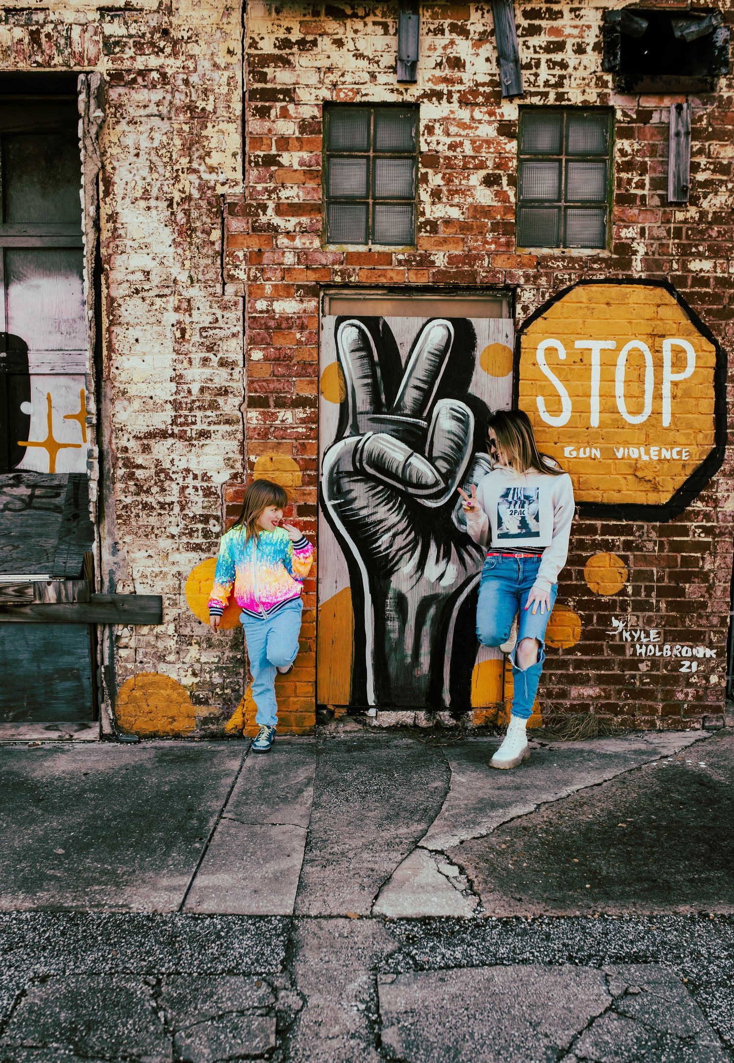 Urban street art featuring a large black peace sign hand symbol painted on weathered brick wall.