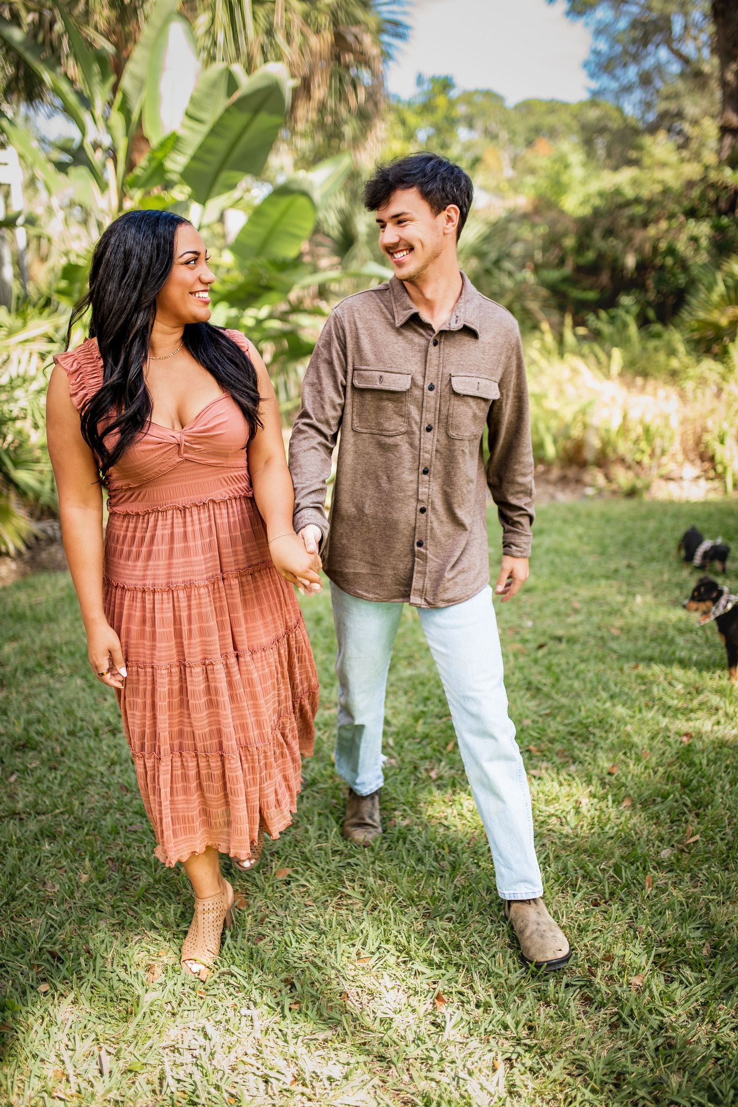 A couple shares a joyful moment while walking together in a lush garden setting, wearing casual summer outfits.