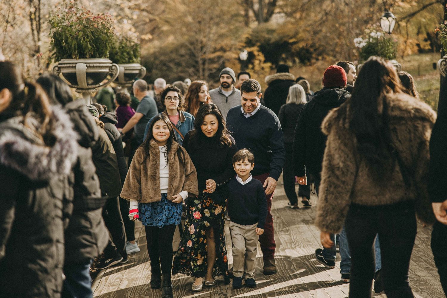 Wedding guests gather outdoors in a rustic setting during an autumn celebration with warm golden lighting.