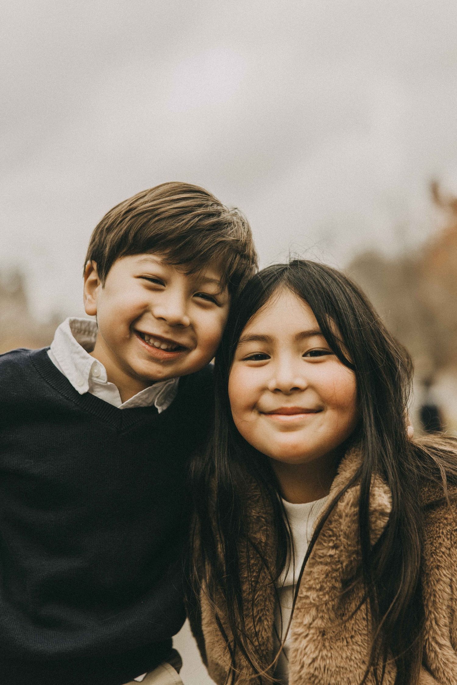Two young children share playful laughter and smiles together in a warm autumn setting.
