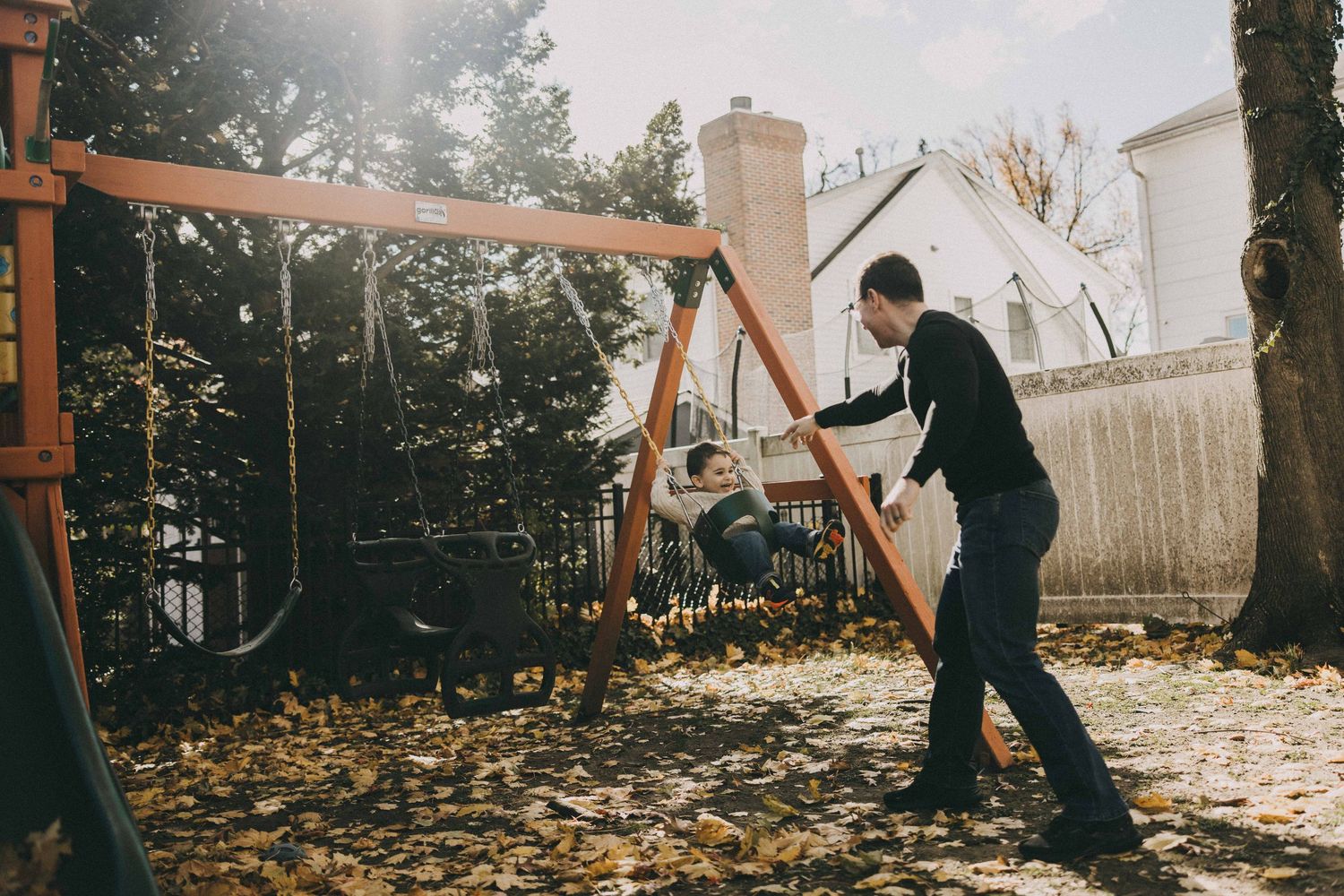A figure practices martial arts movements with a wooden staff in a backyard during autumn at sunset.