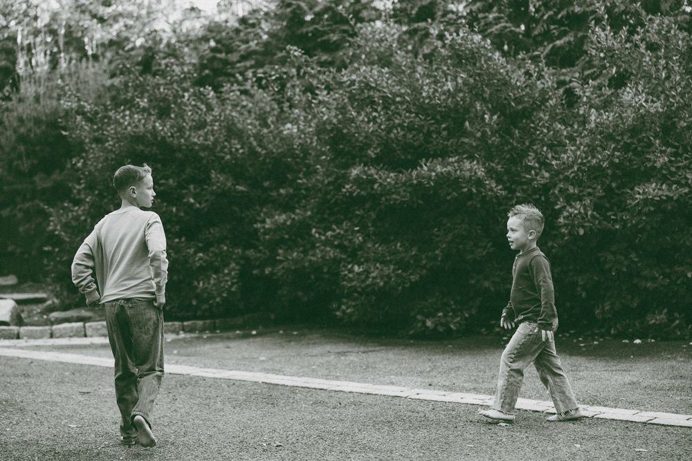 Two young boys walking on a path surrounded by lush green trees in a black and white outdoor photo.