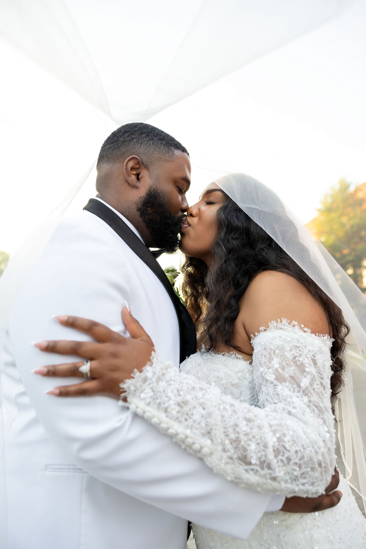 A joyful wedding couple shares an intimate moment in a romantic outdoor setting with pink bouquet and elegant attire.
