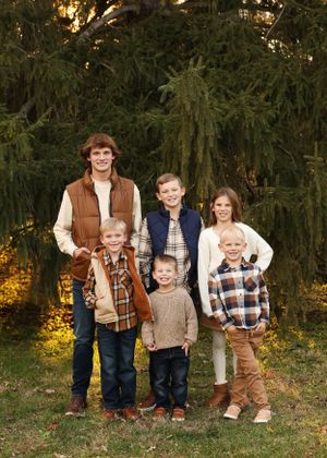 Family group poses together in coordinating fall outfits near evergreen trees at sunset.