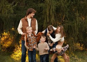Family plays and laughs together during outdoor photo session near pine trees.