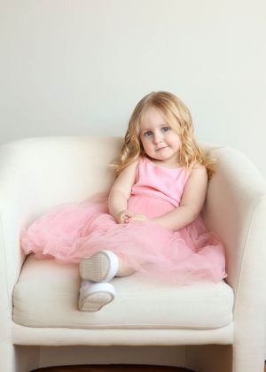 Child in pink dress lounges gracefully on white couch during photo session.