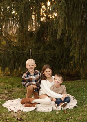 Three children sit together on blanket during outdoor fall photo session.