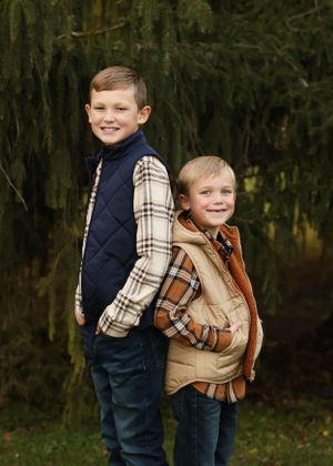 Two siblings in coordinated outfits pose together in woodland setting during autumn photo session.