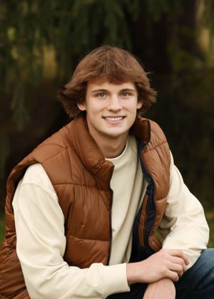 Person in brown vest and cream sweater poses casually outdoors during golden hour photo session.