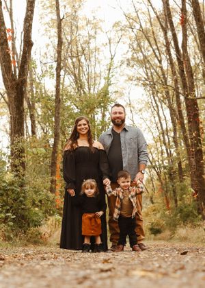 A family stands together on fallen autumn leaves in a wooded area.