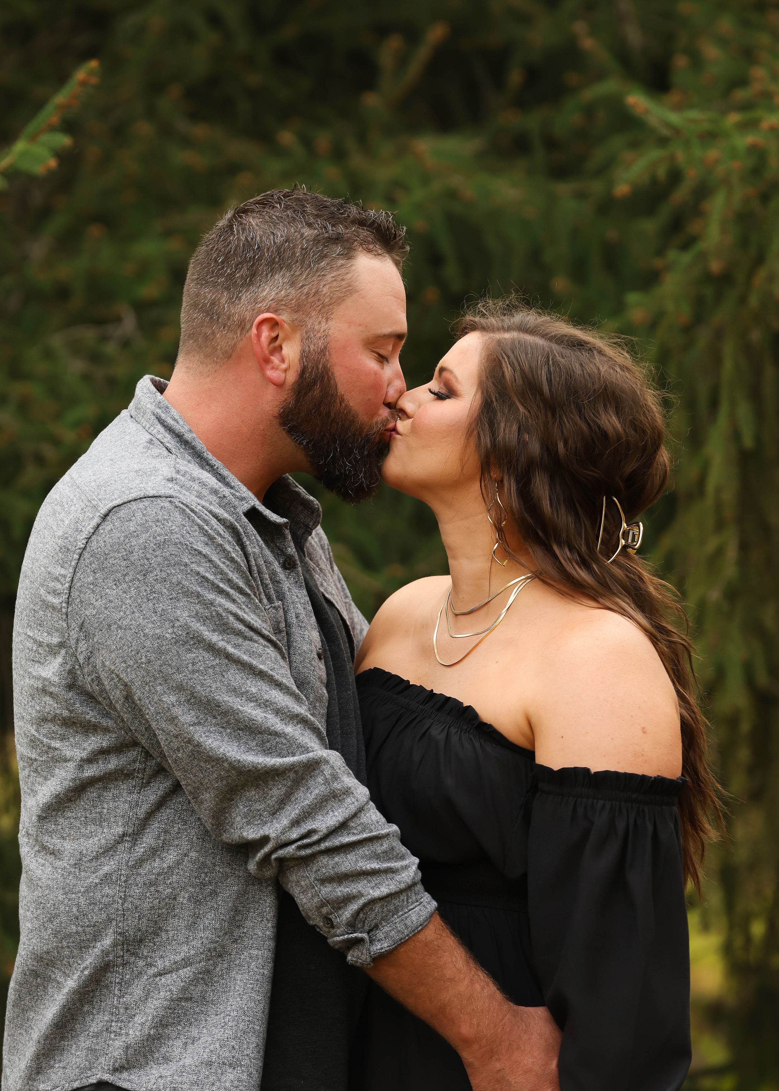 A romantic couple shares tender moments together against a backdrop of evergreen trees.