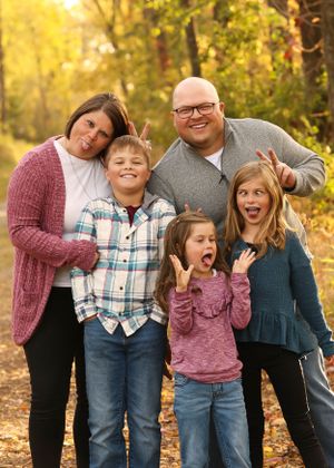 Playful family portrait with silly expressions in autumn outdoor setting.