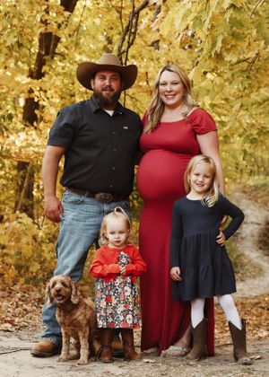 A family poses together with their brown dog in an autumn setting with golden leaves in the background.