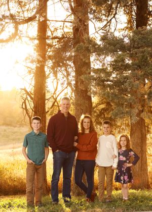 Extended family gathering posed under tall pine trees during golden sunset.