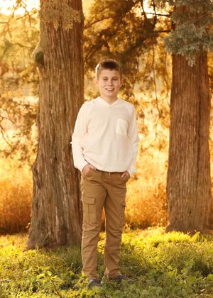 Casual outdoor portrait session among trees with golden sunlight filtering through.