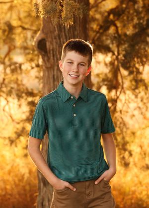 Portrait in green striped polo shirt against golden sunset and forest backdrop.