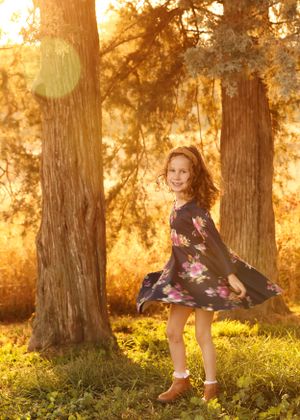 Playful poses in floral dress against sunlit forest background during golden hour.
